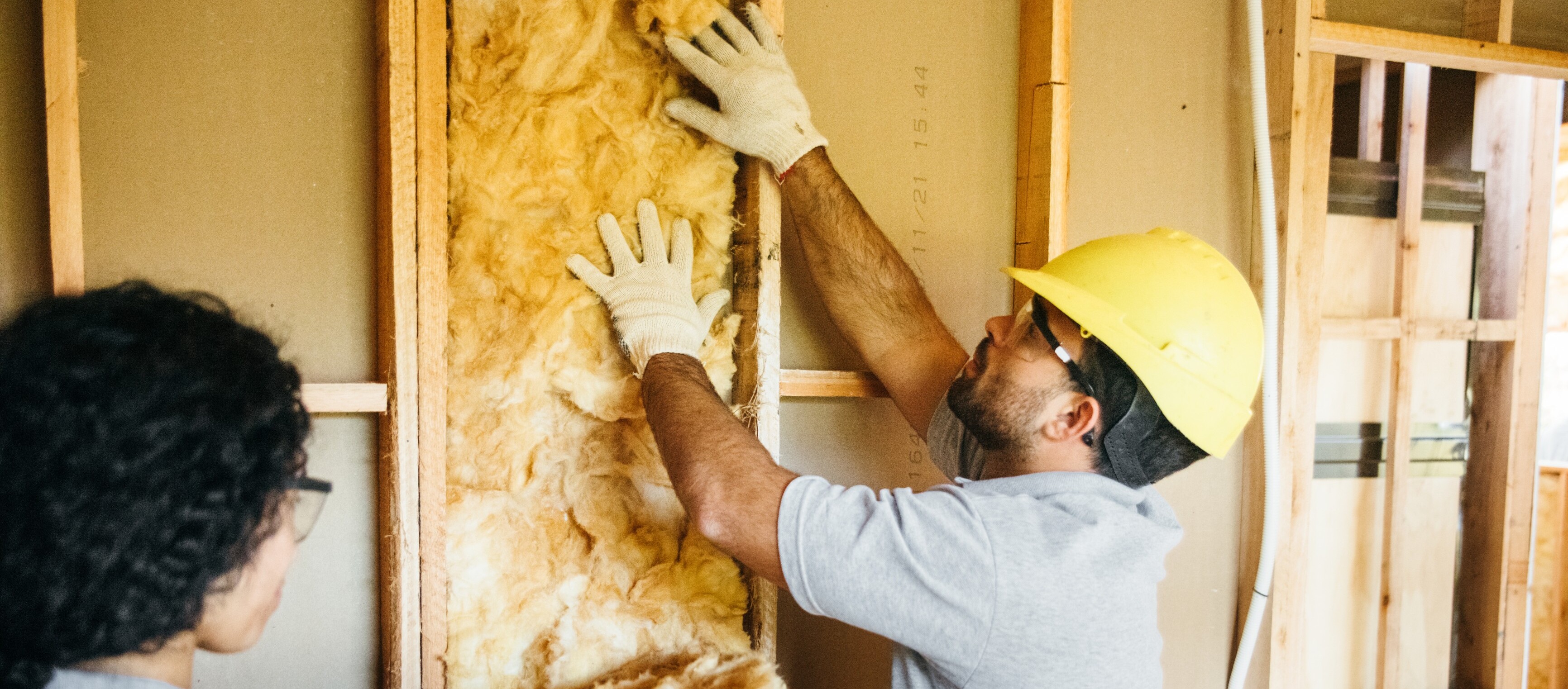 Zwei Arbeiter installieren Dämmmaterial in eine Wand.