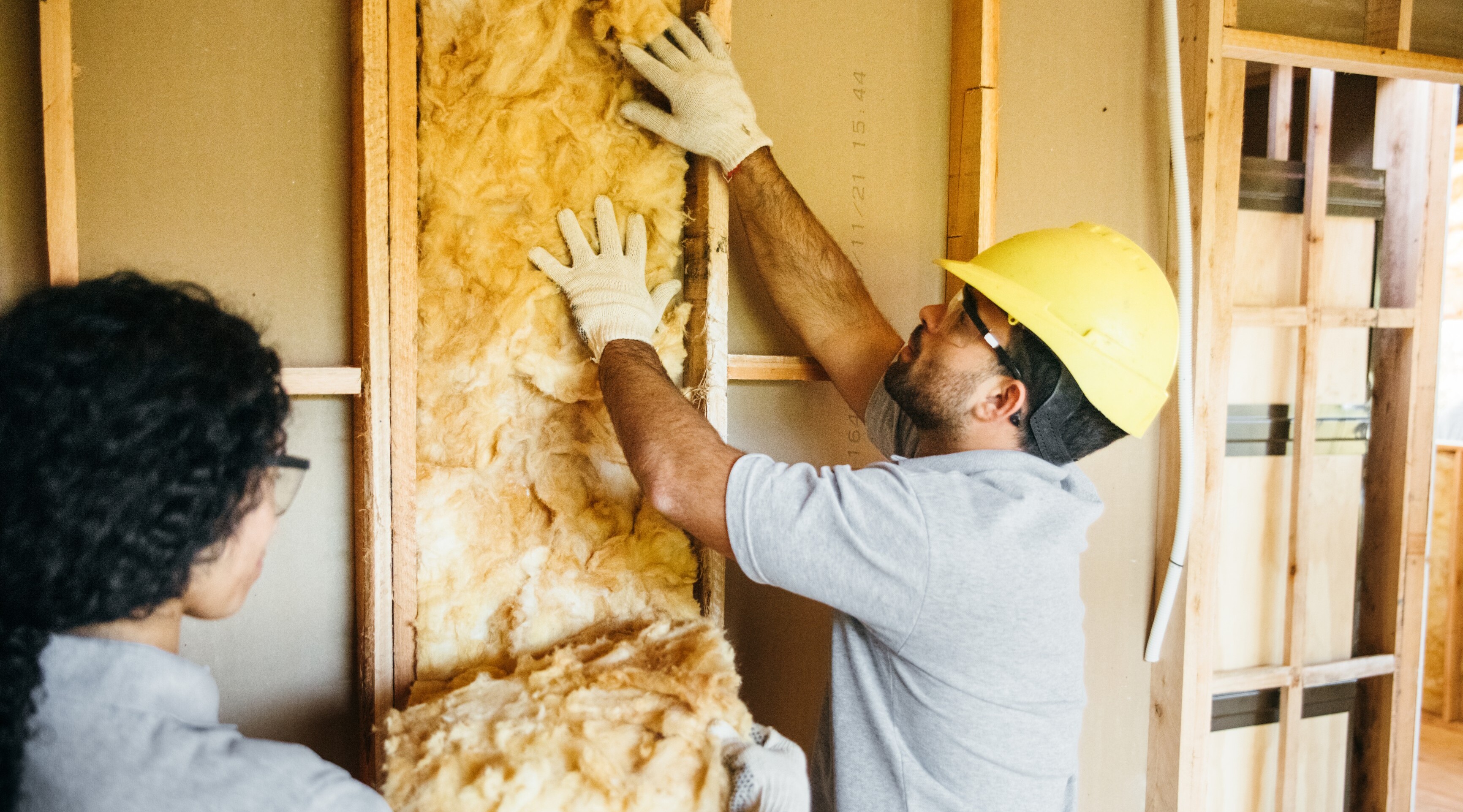 Zwei Arbeiter installieren Dämmmaterial in eine Wand.